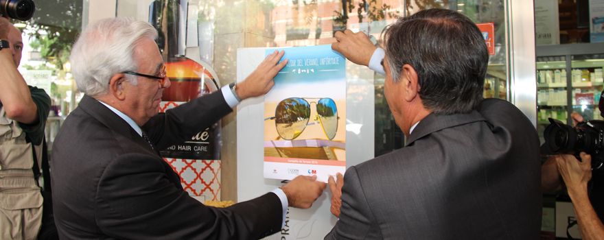 Jesús Sánchez Martos, pega, junto a Luis González, uno de los carteles informativos de la campaña de farmacias.